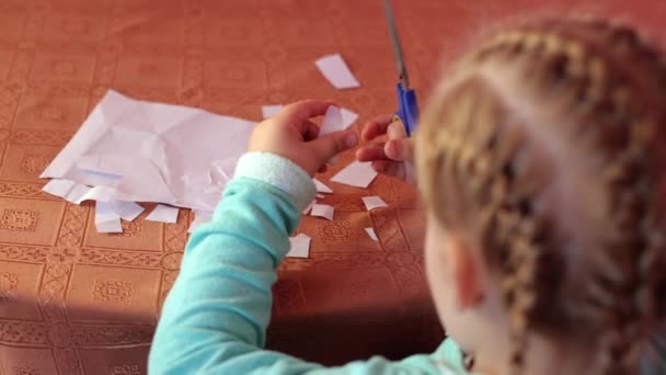子供はハサミで紙を切っている 小さな女の子が座って白い紙を切っている 未就学児はハサミと一緒に働くことを学ぶ 自宅での就学前教育プログラム 子供の育成 創造性 — ストック動画