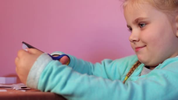Uma Criança Corta Papel Com Tesoura Uma Menina Está Sentada — Vídeo de Stock