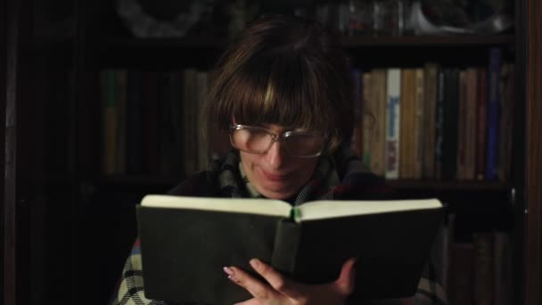 一个女人在看书 背后有很多书 他戴着滑稽眼镜 在家里学习文学 聪明的女孩手里拿着一本书 复古风格的特写 — 图库视频影像
