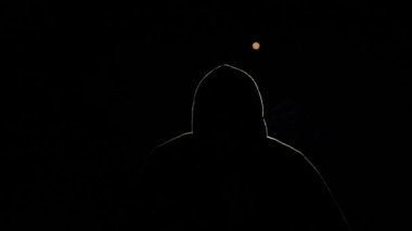 Siyah arka planda bir kişinin silueti. Kapüşonlu bir adam, ışıkla aydınlatılmış, patlar. Gecenin bir hackerı, yüzü görünmeyen gizemli bir insan. Bir sigara içiyor.