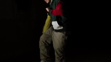 Hip hop dansı silueti. Karanlıkta dans eden, geceleri dans eden bir çocuk. İnsanlar dinamik hareketler yapar, modern tarzda. El fenerinin ışığı, evin yakınındaki şehirde dans ediyor.