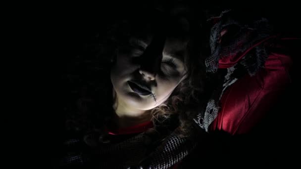 ハロウィーンスタイルのブルネットガール 黒い背景の女性 彼女の顔に明るい光 怖いシーン 恐ろしい闇 うつ病 苦しみ ブラックカーニバル 地下室 — ストック動画