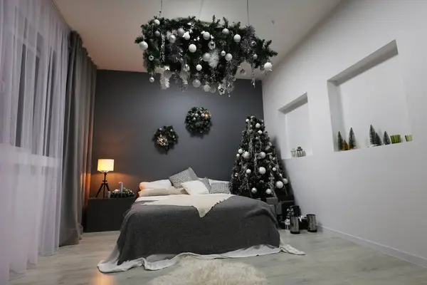 Interior of a festive New Year\'s room. Christmas atmosphere, bed and Christmas tree, gray wall. Happy New Year at home. Nice apartment, modern premises