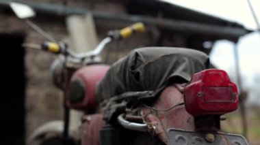 Eski motosiklet toz içinde. Kırmızı retro moto. Arızalı motosiklet, tamire ihtiyacı var. Kirli bir kırsal benzinli motosiklet, hemen yanındaki çöplükte.