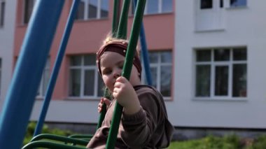 Küçük bir kız çocuk parkında oynuyor. Halka açık bir yerde eğlence. Çocuk temiz havada dinleniyor. Bir salıncakta sallanıyor