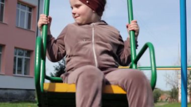Küçük bir kız çocuk parkında oynuyor. Halka açık bir yerde eğlence. Çocuk temiz havada dinleniyor. Bir salıncakta sallanıyor