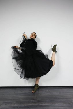 Beyaz arka planda balerin, siyah bir elbise giyiyor. Esmer bir kız kameranın önünde poz veriyor. Güzel dansçı, siyah beyaz stili..