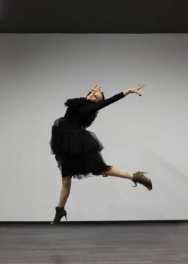 Beyaz arka planda balerin, siyah bir elbise giyiyor. Esmer bir kız kameranın önünde poz veriyor. Güzel dansçı, siyah beyaz stili..