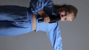 Küçük bir kız mikrofon tutarken şarkı söylüyor. Sarışın, mavi takım elbiseli güzel bir aktris. Çocuklar için karaoke, genç şarkıcı