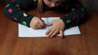 Çocuk evde yazmayı öğreniyor, bir harf çiziyor. Kız harfleri yuvarlak içine alıyor, ilk defa yazıyor. Bir anaokulu öğrencisi masada yazmayı öğrenir.
