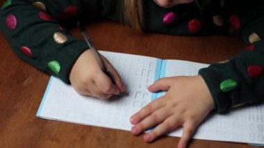 Çocuk evde yazmayı öğreniyor, bir harf çiziyor. Kız harfleri yuvarlak içine alıyor, ilk defa yazıyor. Bir anaokulu öğrencisi masada yazmayı öğrenir.