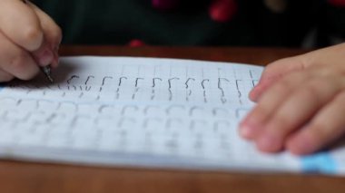 Çocuk evde yazmayı öğreniyor, bir harf çiziyor. Kız harfleri yuvarlak içine alıyor, ilk defa yazıyor. Bir anaokulu öğrencisi masada yazmayı öğrenir.