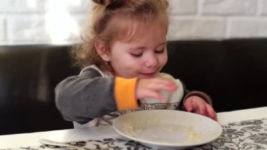 Kıvırcık bir kız yemek yemeyi öğreniyor, makarna yiyor. Çocuk elleriyle yer, her şeyi bitirir. Aç bir çocuk öğle yemeği yer. Güçlü bir iştahı var, her şeyin tadını alıyor.