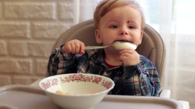 Küçük yakışıklı çocuk yemek yemeyi öğreniyor, patates ve havuç yiyor. Çocuk elleriyle yemek yiyor. Çocuk çocuk masasında öğle yemeği yiyor. Her şeyin tadına bakar.