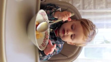 Küçük yakışıklı çocuk yemek yemeyi öğreniyor, patates ve havuç yiyor. Çocuk elleriyle yemek yiyor. Çocuk çocuk masasında öğle yemeği yiyor. Her şeyin tadına bakar.