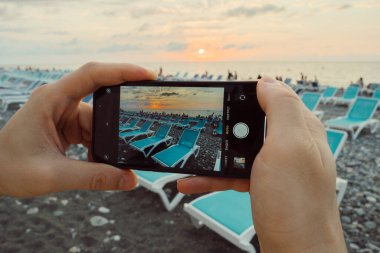 Gün batımında bir adam akıllı telefonuyla plajı fotoğraflıyor. Yüksek kalite fotoğraf