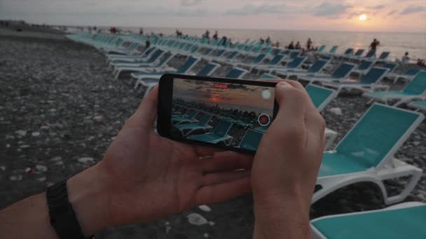 Een Man Fotografeert Het Strand Bij Zonsondergang Met Een Smartphone — Stockvideo
