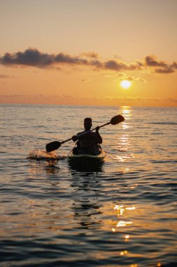 Bir adam gün batımında bir SUP sörf tahtasıyla denize açılacak. Yüksek kalite fotoğraf