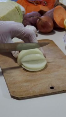 Sıcak bir mutfakta bir insan ahşap bir kesme tahtasının üzerinde soğan doğruyor. Taze sebzeler ve meyveler, canlı bir atmosfer sunuyor. Yemek pişirmek için mükemmel. Bu süreç yemek hazırlığını vurgular.