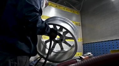Yetenekli bir birey, iyi aydınlatılmış bir atölyede metal bir tekerleği dikkatlice restore ediyor. İşçi titiz bir şekilde detaylandırmaya odaklanırken, araçlar ve ekipmanlar çalışma alanını çevreler..