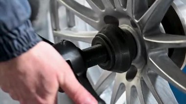 Özel bir araç kullanılarak gümüş alaşımlı kenardan tekerleği çıkarmanın detaylı bir gösterimi, araba bakımı meraklıları için mükemmel..