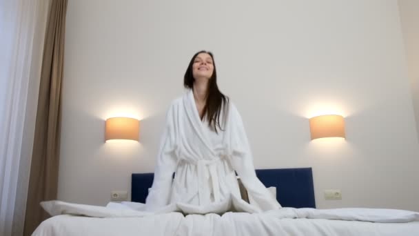Gelukkig Jonge Brunette Vrouw Witte Badjas Glimlachend Springen Bed Hotelkamer — Stockvideo