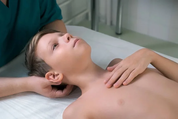 Session of craniosacral therapy, cure of teen boys back of the head and neck by a doctor therapist. Craniosacral therapist touches boys head and corrects spine at hospital. Boy is lying on couch.