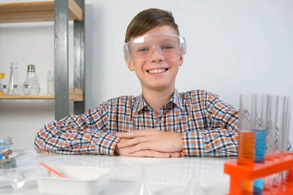 戴着防护眼镜的快乐少年坐在化学实验室的桌旁 在线教育 家庭教育和科学概念 幼儿时期的科学活动 — 图库照片