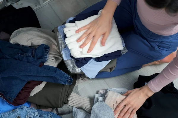 Woman puts things in order in her closet by folding clothes neatly. She is sitting on the floor and sorting through her clothes. The housewife tidies up the closet in the dressing room.