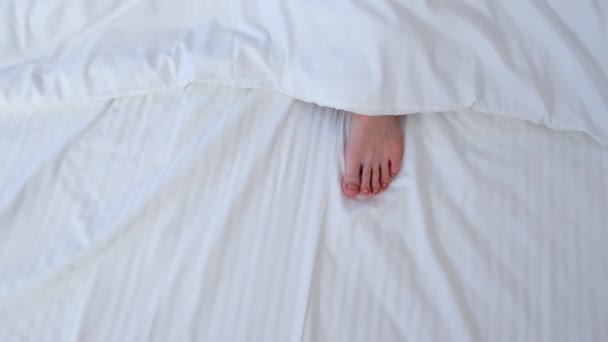 Womans Menggerakkan Kaki Menyembunyikannya Bawah Selimut Antara Kain Linen Putih — Stok Video