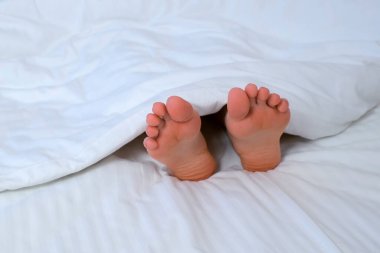 Kadınlar yalınayak hareket ediyor, beyaz çarşafların arasında rahat bir yatakta ayaklarını tırmalıyor, o battaniyenin altında uyuyor. Sağlıklı uyku ve rahatlama, tembel sabah konsepti. Tatil, otel konseptinde dinlenme..