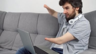 Özürlü bir adam, iki kolu kesilmiş, evinde, kanepede oturmuş bilgisayardan video görüşmesi yapıyor. Engelli insanlara uyum sağlama sorunu. Bağımsız Bağımsız kişi.