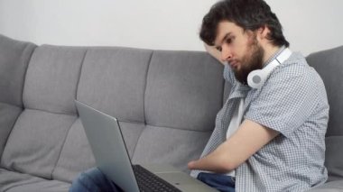 Özürlü bir adam, iki kolu kesilmiş, dizüstü bilgisayarda oturuyor ve kanepeye oturuyor. Engelli insanlara uyum sağlama sorunu. Bağımsız Bağımsız kişi.