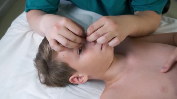 颅骨治疗 由医生治疗少男鼻腔 颅骨治疗师摸到男孩的鼻子 在医院用手检查鼻子的矫正情况 侧视脸部 — 图库视频影像