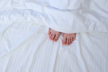 Ayaklarını hareket ettiren kadınlar battaniyenin altında beyaz çarşafların arasına saklıyorlar. Sağlıklı uyku ve rahatlama, tembel sabah konsepti. Tatil, otel konseptinde dinlenme. Pedikür ve pembe tırnaklı kızlar.