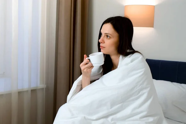 Задумчивая Сонная Молодая Брюнетка Завернутая Одеяло Пьет Чай Кофе Сидя — стоковое фото