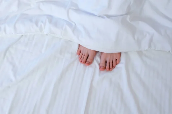 stock image Womans moving feet hiding it under blanket in bed among white linen. Healthy sleep and relaxation, lazy morning concept. Vacation, resting in hotel concept. Girls feet with pedicure and pink nails.