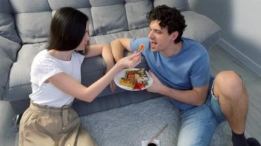 Genç mutlu çift kadın ve erkek oturma odasında suşi yiyorlar. Kanepenin yanında yerde oturuyorlar, kadın adamı besliyor. Japon ve Çin yemekleri ve eve servis..