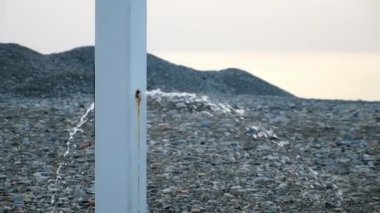Mevsim dışında deniz çakıl taşlı kumsalda, bulutlu bir havada kırık bir sağanak. Gün batımında çakıl taşının ortasından tatlı su her iki taraftan da akıyor. Turistler için plaj düzenlemesi.