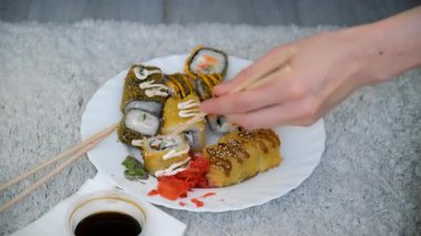 Genç bir kadın oturma odasında ahşap çubuklarla suşi yiyormuş, elleri yakınmış. Japon ve Çin yemekleri ve eve servis..