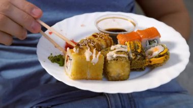 Genç adam oturma odasında ahşap çubuklarla suşi yiyormuş, elleri yakınmış. Japon ve Çin yemekleri ve eve servis..