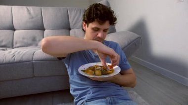 Gülümseyen genç adamın portresi oturma odasında elle suşi yiyip kameraya bakmaktır. Japon ve Çin yemekleri ve eve servis. Kanepenin yanında oturuyor..