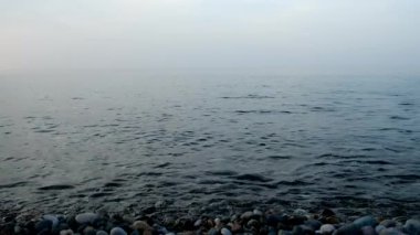 Küçük çakıl taşları olan çakıl taşı plajı ve deniz üzerinde sis olan sakin deniz yüzeyi. Sessiz bir akşam. Doğa inanılmaz güzel manzara. Sahilde dinlenme ve dinlenme yeri.