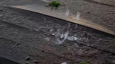 Sokaktaki kırık borudan akan su ve ahşap platformda su birikintisi. Elektrik sistemlerinde bozulma, kaza, su sızıntısı, kırık hortum, boru. Yerdeki su birikintisi ve dışarıdaki çakıl taşları..