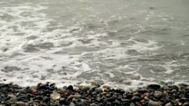 Fırtınada Karadeniz kıyısındaki çakıl taşlı plajlara köpüklü uzun deniz dalgaları çarpıyor. Fırtınalı havada dalgalar taşlara vuruyor. Fırtınalı su yüzeyi. Mistik deniz manzarası, kıyı şeridinde dalgalar var..