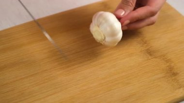 Mutfaktaki tahta tahtada bıçak kullanarak sarımsak kesen bir kadının elleri. Yemek hazırlamak, evde yemek. Yemek tabağı. Mutfak, mutfak, taze ürünlerle yemek pişirme, malzeme konsepti..
