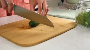 Woman cutting ends of cucumbers to cook pickles salt cucumbers on wooden board on kitchen at home, hands close-up. Cuisine, culinary, prepare cook dish domestic food, recipe, ingredients concept.