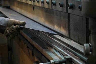 Fabrika işçisi atölyedeki fren makinesini kullanarak metal levhayı büküyor. Metalurji endüstrisi, otomatikleştirilmiş makine üretimi. Fabrika zemininde detaylar ve parçalarla çalışmak.