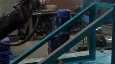 Fabrika zemininde metal çerçeveye sprey tabancayla boya uygulayan bir işçi. Metalurji endüstrisi, üretim imalatı. Metal yapılı fabrika üzerinde endüstriyel çalışmalar..