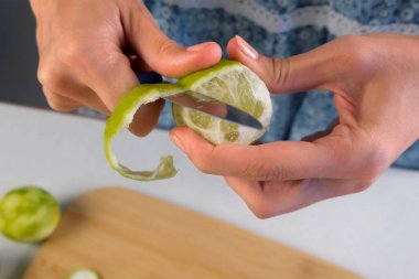 Kadın elleri evde mutfakta bıçak kullanarak kireç meyvesi soyuyordu. Malzeme tarifi aşçılığı. Meyveli turunçgil tatlısı, ev yapımı taze içecek, Brezilya limonatası..